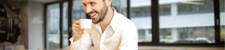 Images shows man at computer, smiling, with coffee